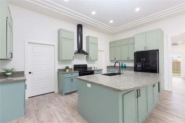 kitchen featuring sink, wall chimney range hood, light hardwood / wood-style flooring, a center island with sink, and black appliances