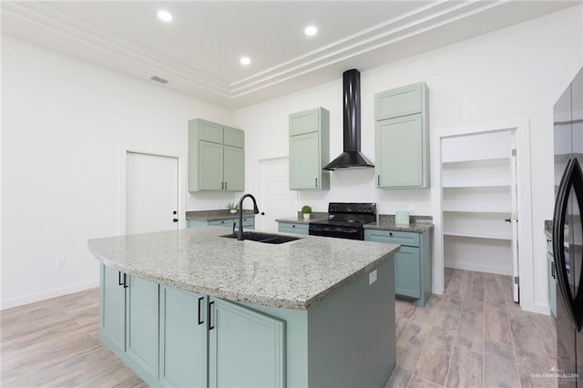 kitchen featuring black electric range oven, wall chimney range hood, sink, light stone countertops, and an island with sink