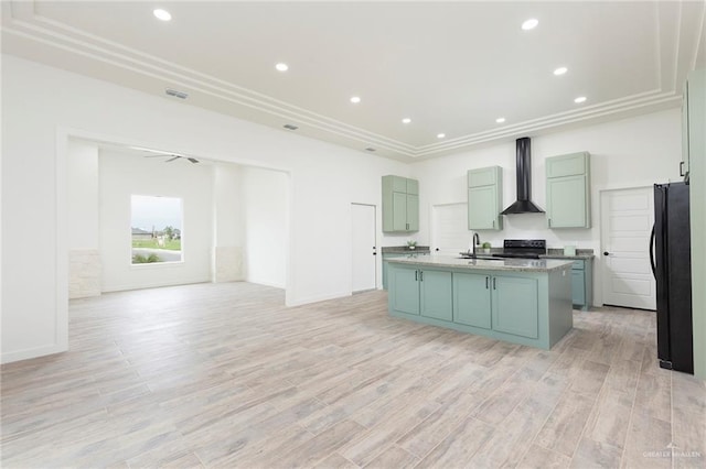 kitchen with light wood-type flooring, wall chimney exhaust hood, a kitchen island with sink, sink, and black appliances