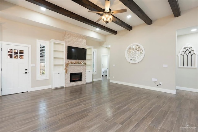 unfurnished living room with ceiling fan, beam ceiling, wood-type flooring, and a brick fireplace