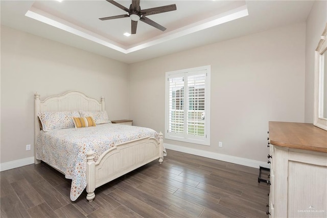 bedroom with dark hardwood / wood-style flooring, a raised ceiling, and ceiling fan