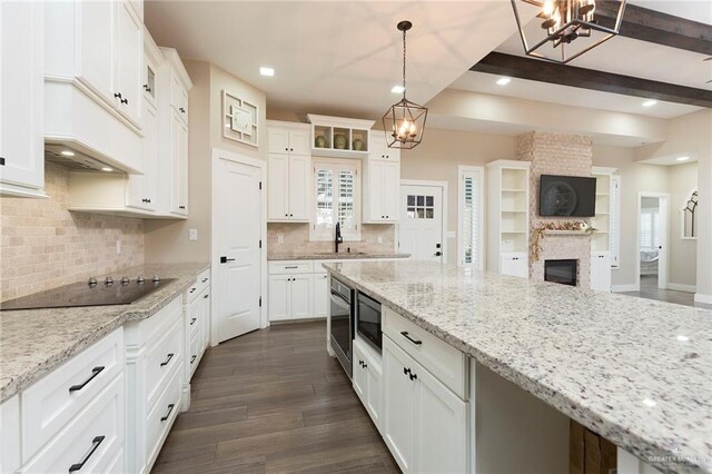 kitchen featuring dark hardwood / wood-style flooring, black electric cooktop, beam ceiling, a fireplace, and hanging light fixtures