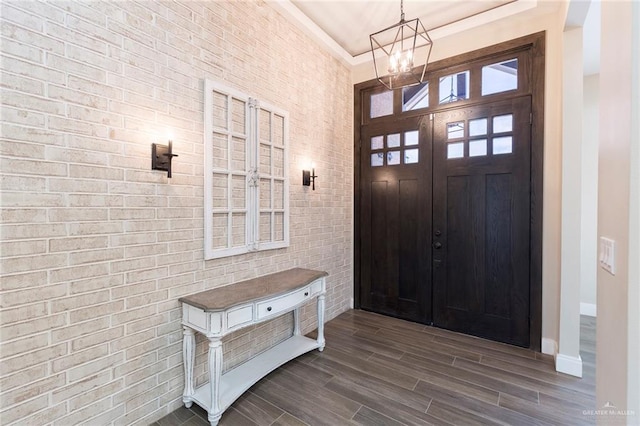 entrance foyer with a notable chandelier, wood-type flooring, ornamental molding, and brick wall