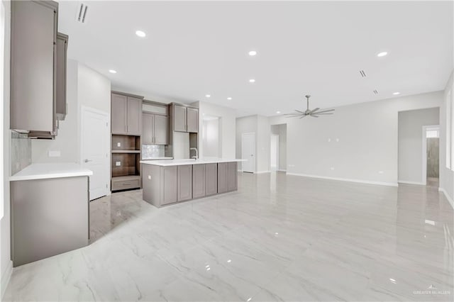 kitchen featuring gray cabinets, a kitchen island with sink, ceiling fan, tasteful backsplash, and marble finish floor