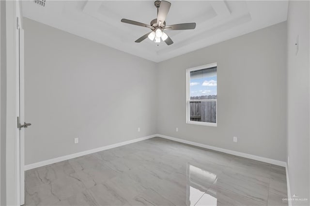 spare room with baseboards, ceiling fan, a tray ceiling, and marble finish floor