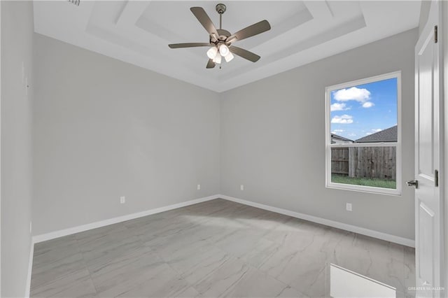 unfurnished room featuring baseboards, ceiling fan, a tray ceiling, and marble finish floor