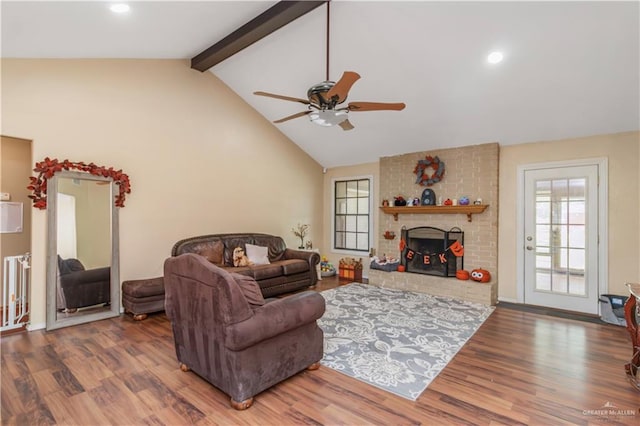 living room featuring beam ceiling, a brick fireplace, ceiling fan, and dark wood-type flooring