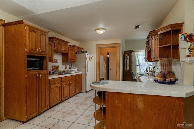 kitchen featuring tile countertops, white refrigerator, kitchen peninsula, and light tile patterned floors