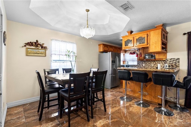 dining area featuring a raised ceiling, sink, a wealth of natural light, and a notable chandelier