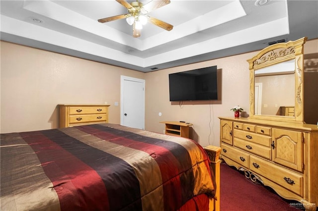 carpeted bedroom with ceiling fan and a tray ceiling