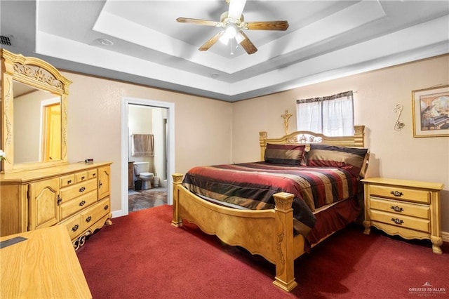 carpeted bedroom with ensuite bathroom, ceiling fan, and a tray ceiling