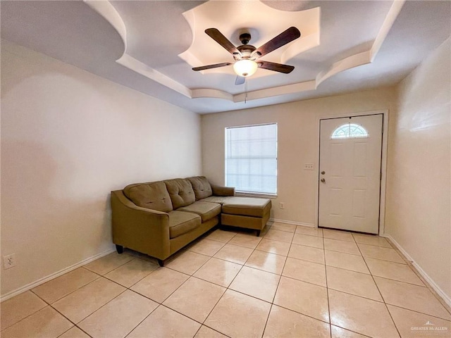 living room featuring a raised ceiling, ceiling fan, and light tile patterned flooring