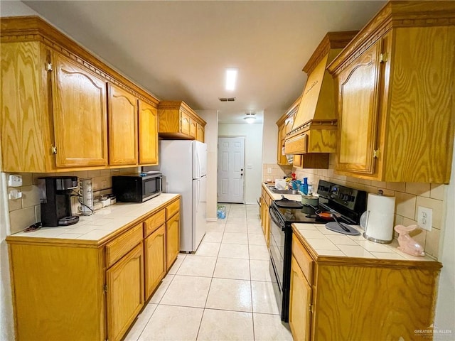 kitchen featuring light tile patterned floors, electric range, white refrigerator, decorative backsplash, and tile countertops