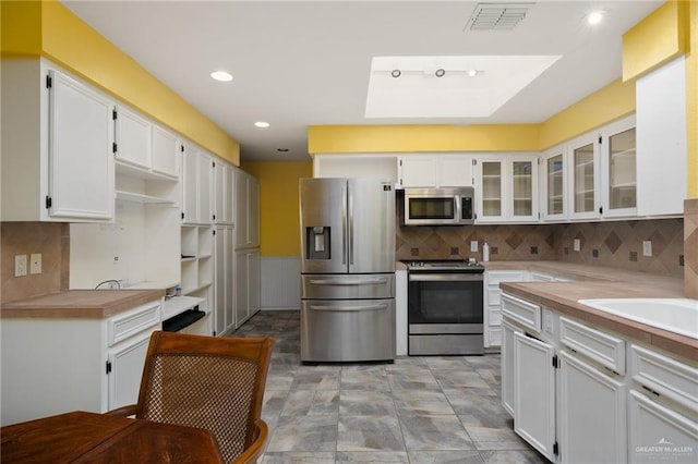 1614 Iowa St, Mission, TX 78572 - kitchen with appliances with stainless steel finishes, white cabinetry, glass insert cabinets, light countertops, and tasteful backsplash