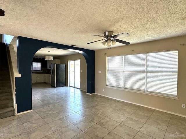 unfurnished room with arched walkways, baseboards, stairs, and ceiling fan