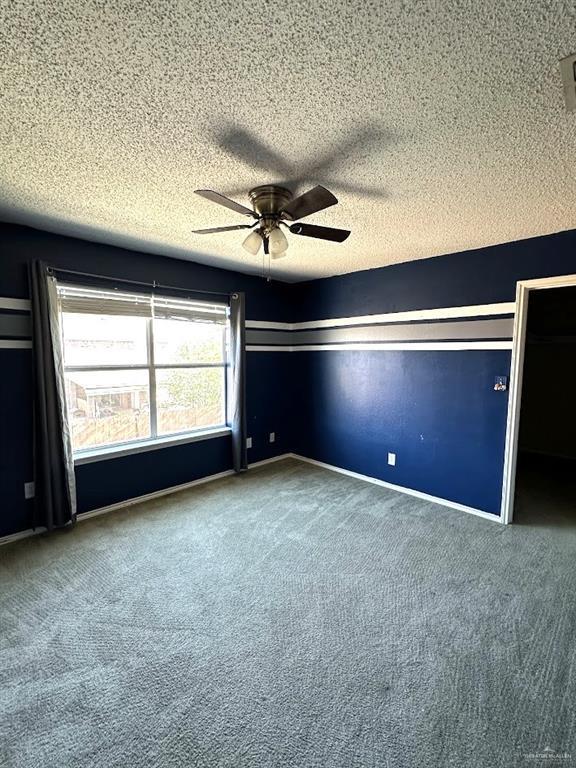 carpeted empty room with baseboards, a textured ceiling, and a ceiling fan