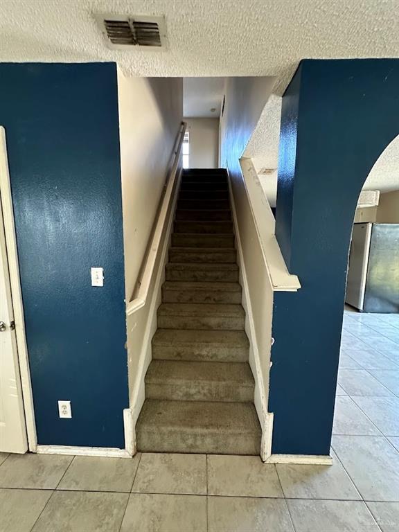 staircase featuring tile patterned floors, visible vents, arched walkways, and a textured ceiling