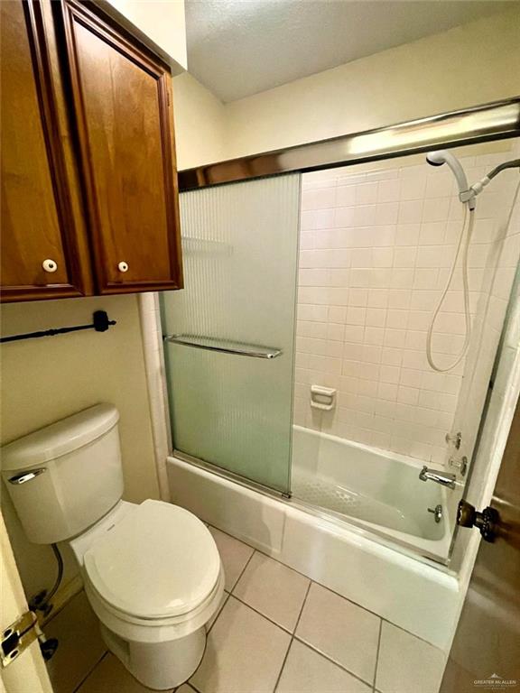 bathroom with toilet, shower / bath combination with glass door, tile patterned flooring, and a textured ceiling