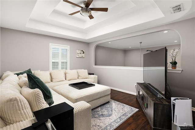 living room featuring visible vents, a raised ceiling, arched walkways, and ceiling fan