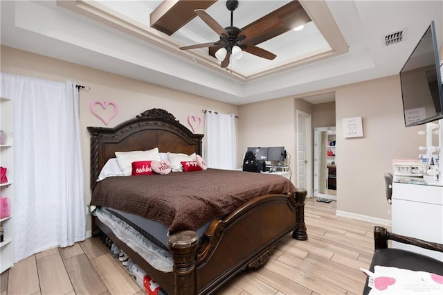 bedroom featuring wood finish floors, a ceiling fan, visible vents, baseboards, and a tray ceiling