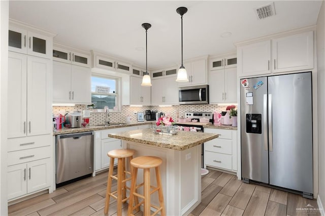 kitchen featuring stainless steel appliances, glass insert cabinets, white cabinets, a kitchen island, and a sink