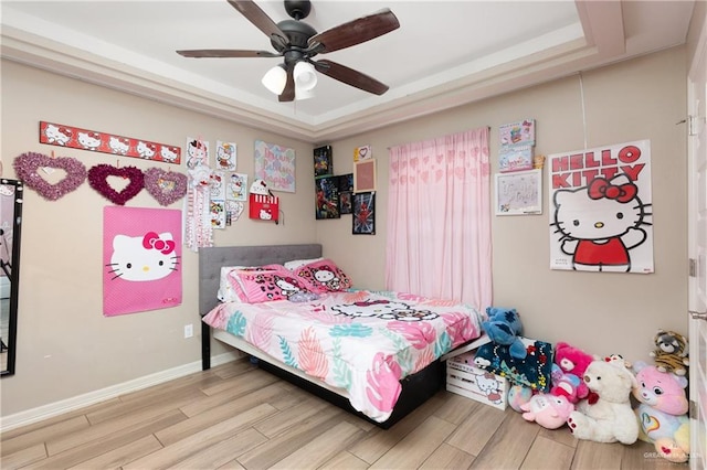 bedroom featuring ceiling fan, a raised ceiling, light wood-style flooring, and baseboards