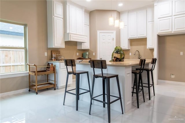 kitchen with a kitchen bar, white cabinetry, light tile patterned flooring, and hanging light fixtures