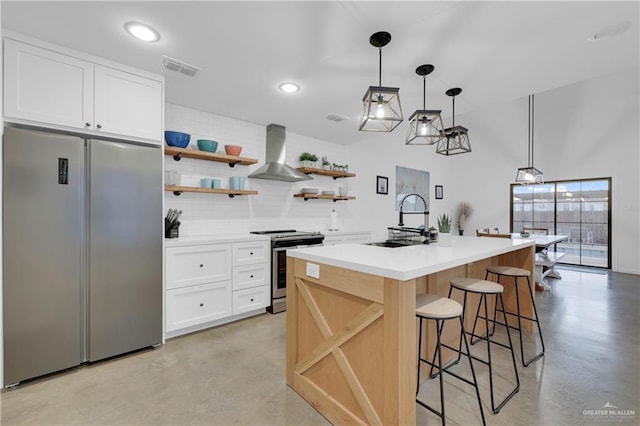 kitchen with white cabinets, appliances with stainless steel finishes, a kitchen island with sink, and wall chimney range hood