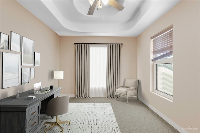 carpeted office featuring a raised ceiling and ceiling fan