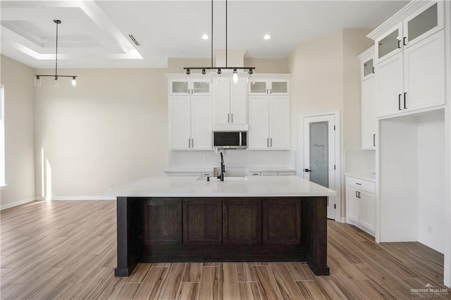 kitchen featuring sink, pendant lighting, light hardwood / wood-style floors, white cabinetry, and an island with sink