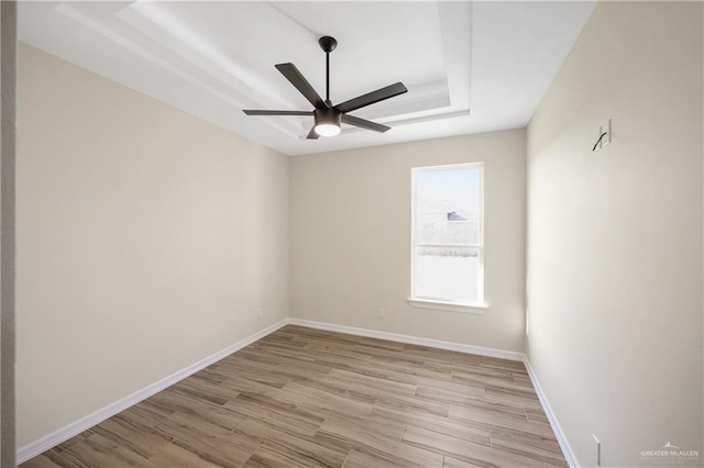 spare room featuring ceiling fan, a tray ceiling, and light hardwood / wood-style flooring