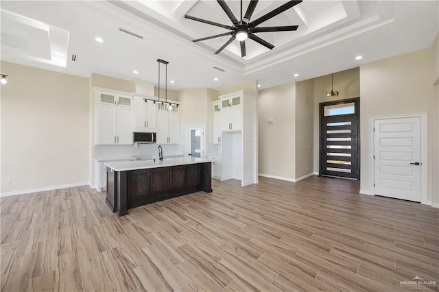 kitchen featuring pendant lighting, a kitchen island with sink, white cabinets, light hardwood / wood-style flooring, and ceiling fan