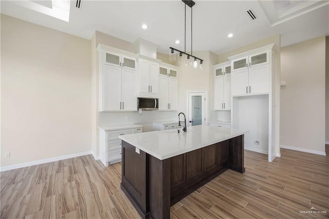 kitchen with white cabinets, light hardwood / wood-style flooring, an island with sink, and decorative light fixtures