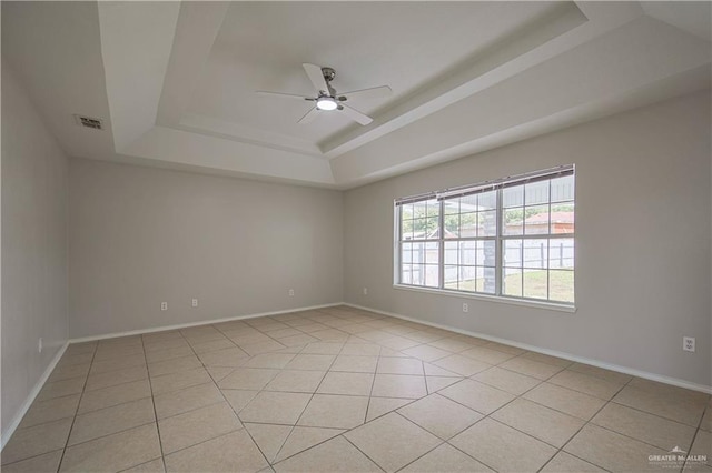 tiled empty room featuring ceiling fan and a tray ceiling