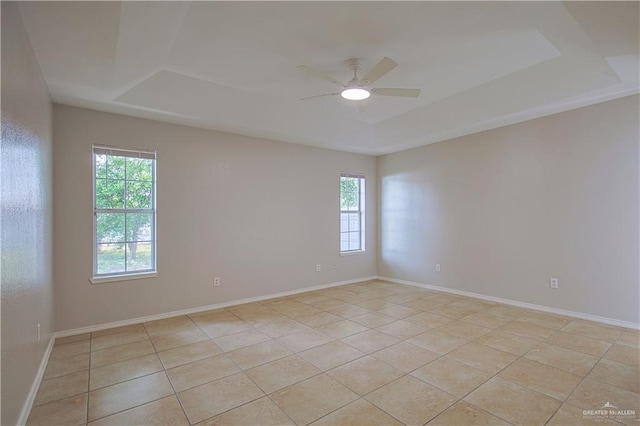 unfurnished room with a raised ceiling, a healthy amount of sunlight, light tile patterned floors, and ceiling fan