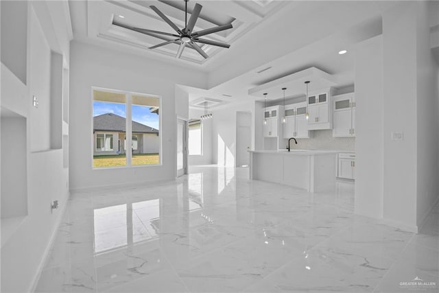 unfurnished living room featuring a high ceiling, coffered ceiling, sink, and ceiling fan