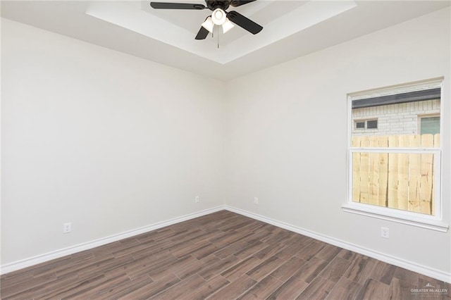 spare room featuring a ceiling fan, baseboards, dark wood-style floors, and a raised ceiling