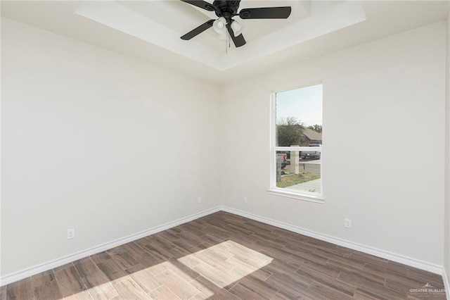 spare room with a raised ceiling, baseboards, dark wood finished floors, and ceiling fan