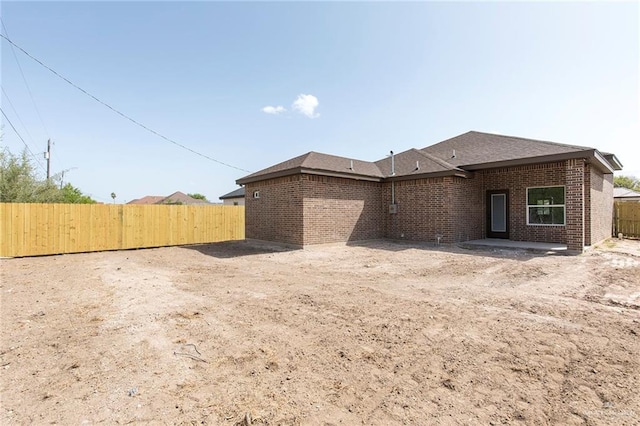 back of property featuring brick siding, a shingled roof, and fence