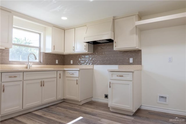 kitchen with sink, tasteful backsplash, white cabinets, custom range hood, and light wood-type flooring