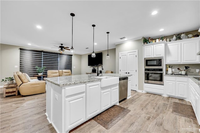 kitchen with pendant lighting, sink, stainless steel appliances, white cabinets, and a center island with sink