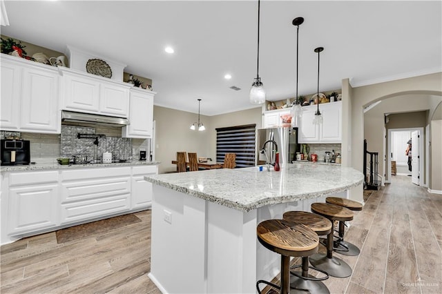 kitchen with decorative light fixtures, light stone countertops, an island with sink, and white cabinets