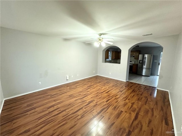 unfurnished living room featuring arched walkways, a ceiling fan, visible vents, baseboards, and light wood finished floors