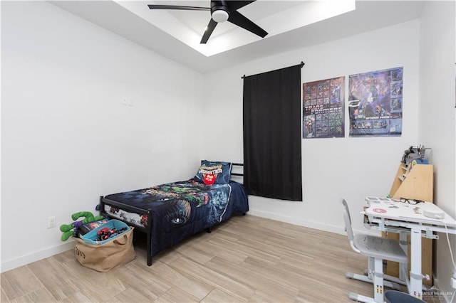 bedroom with a tray ceiling, wood finished floors, a ceiling fan, and baseboards