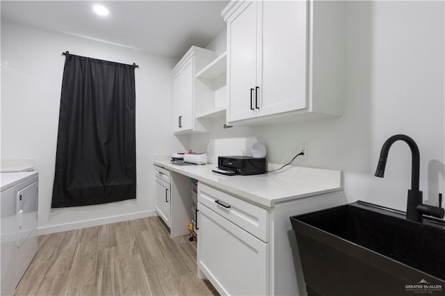 kitchen featuring open shelves, washing machine and dryer, white cabinetry, a sink, and light wood-type flooring