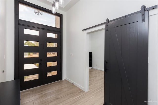 foyer entrance with light wood-style floors, french doors, baseboards, and a barn door