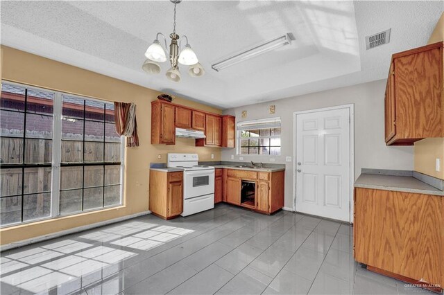 1101 Boston St, Edinburg, TX 78541 - kitchen featuring under cabinet range hood, white range with electric stovetop, light countertops, brown cabinetry, and a notable chandelier