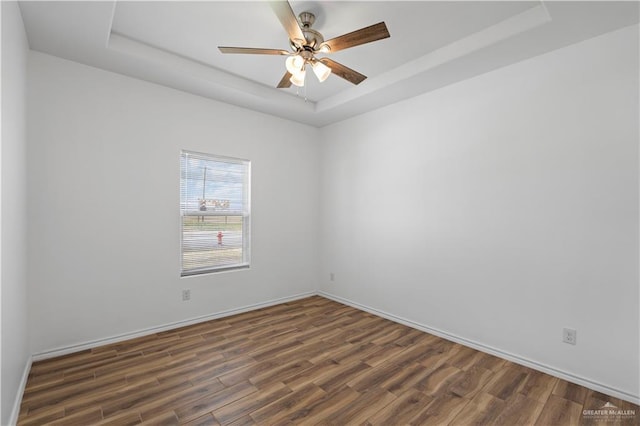 spare room with dark hardwood / wood-style flooring, a raised ceiling, and ceiling fan