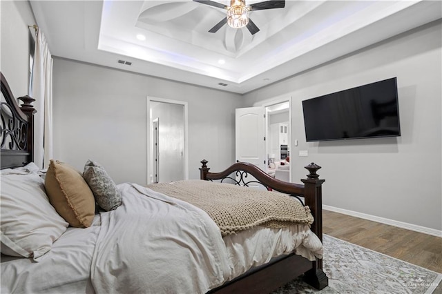 bedroom with hardwood / wood-style flooring, a raised ceiling, and ceiling fan