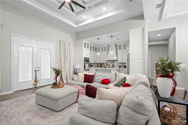 living room featuring ceiling fan, french doors, a raised ceiling, light hardwood / wood-style flooring, and a towering ceiling